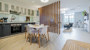 Una cocina moderna con armarios blancos, un comedor con mesa y sillas blancas, y una sala de estar con sofá y una mesita de centro.