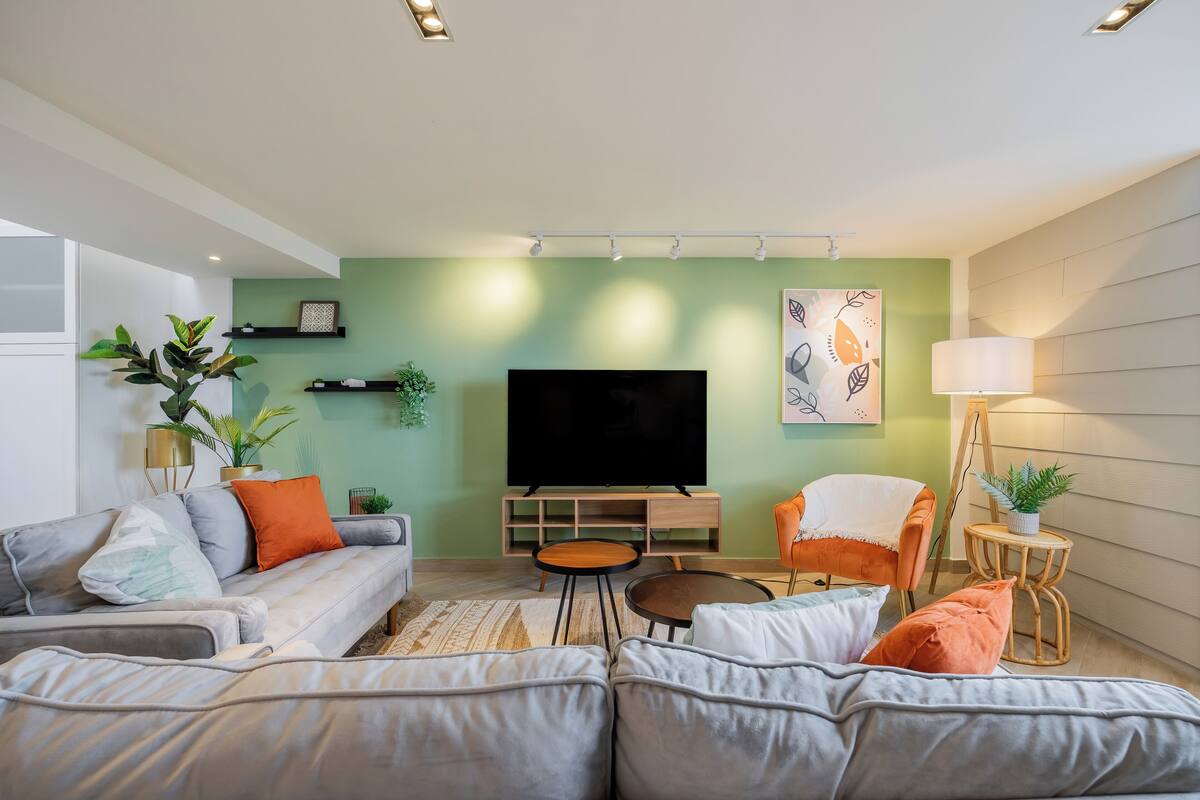 A modern living room with a grey sectional sofa, a flat-screen TV, a small round coffee table, and a side table with a lamp.