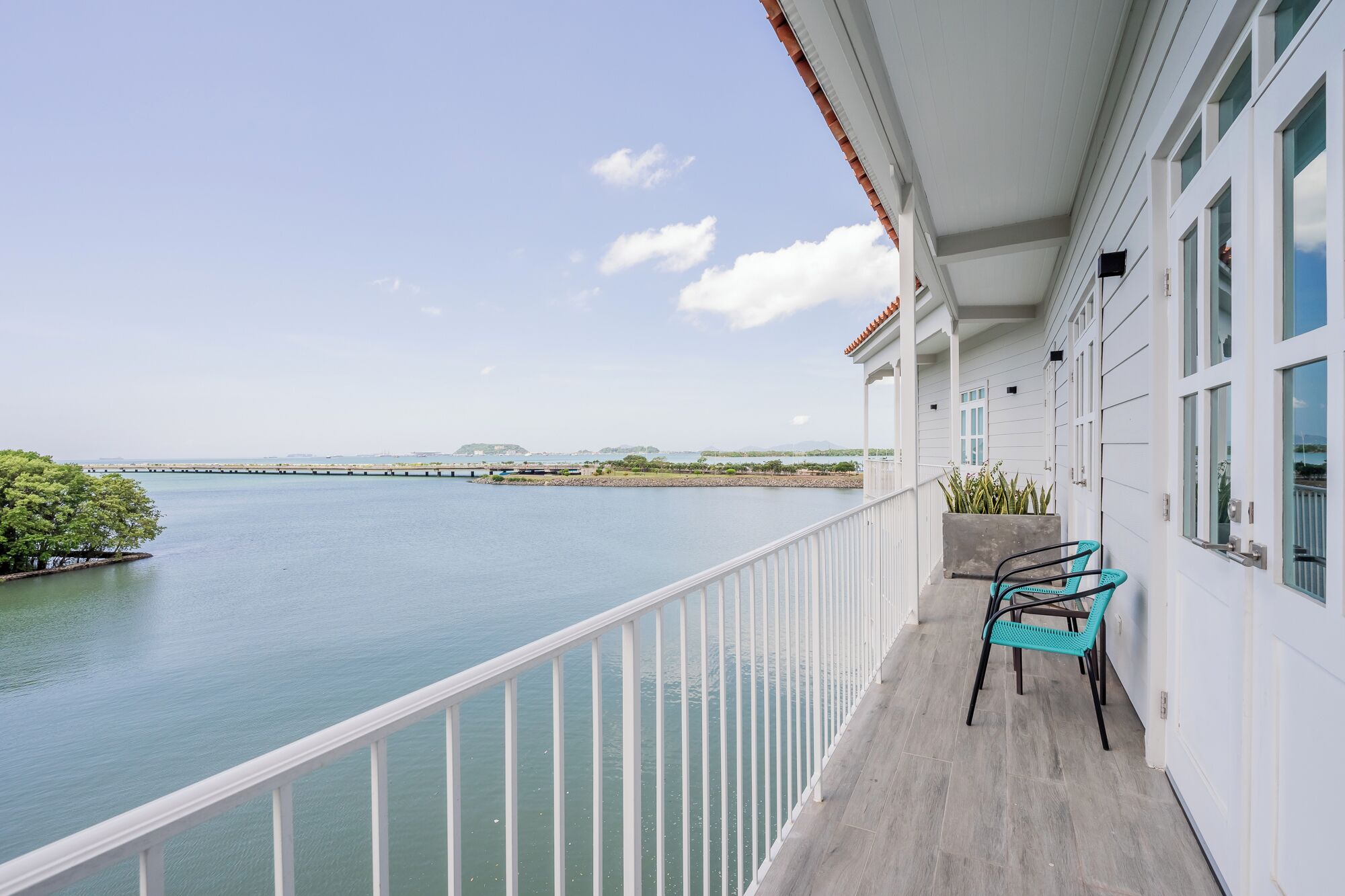A balcony with a view of a calm body of water, a distant bridge, and a clear sky.