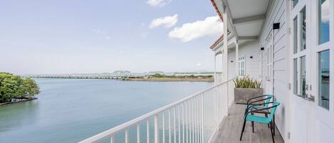A balcony with a view of a calm body of water, a distant bridge, and a clear sky.