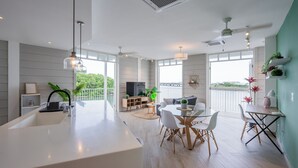 Una cocina moderna con una isla grande, comedor con sillas blancas y vistas a zonas verdes.