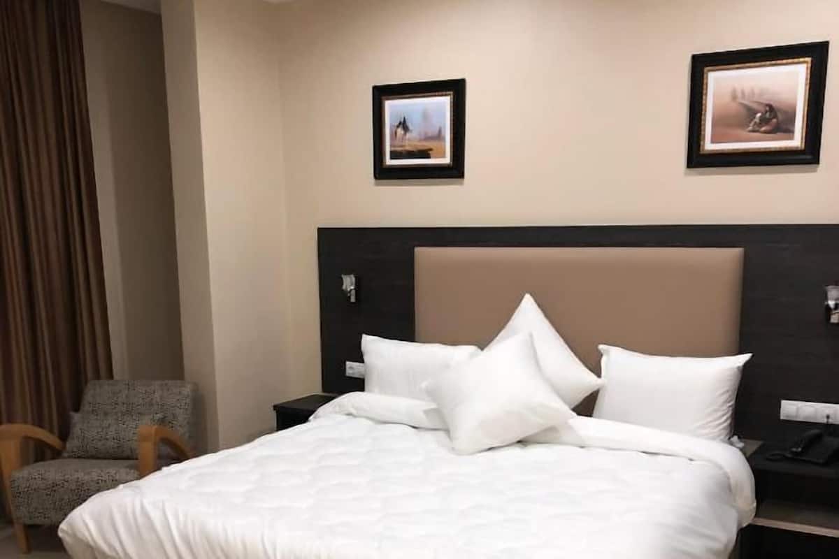 Ein modernes Hotelzimmer mit einem großen Bett, zwei Nachttischen, einem Sessel und zwei gerahmten Bildern an der Wand.