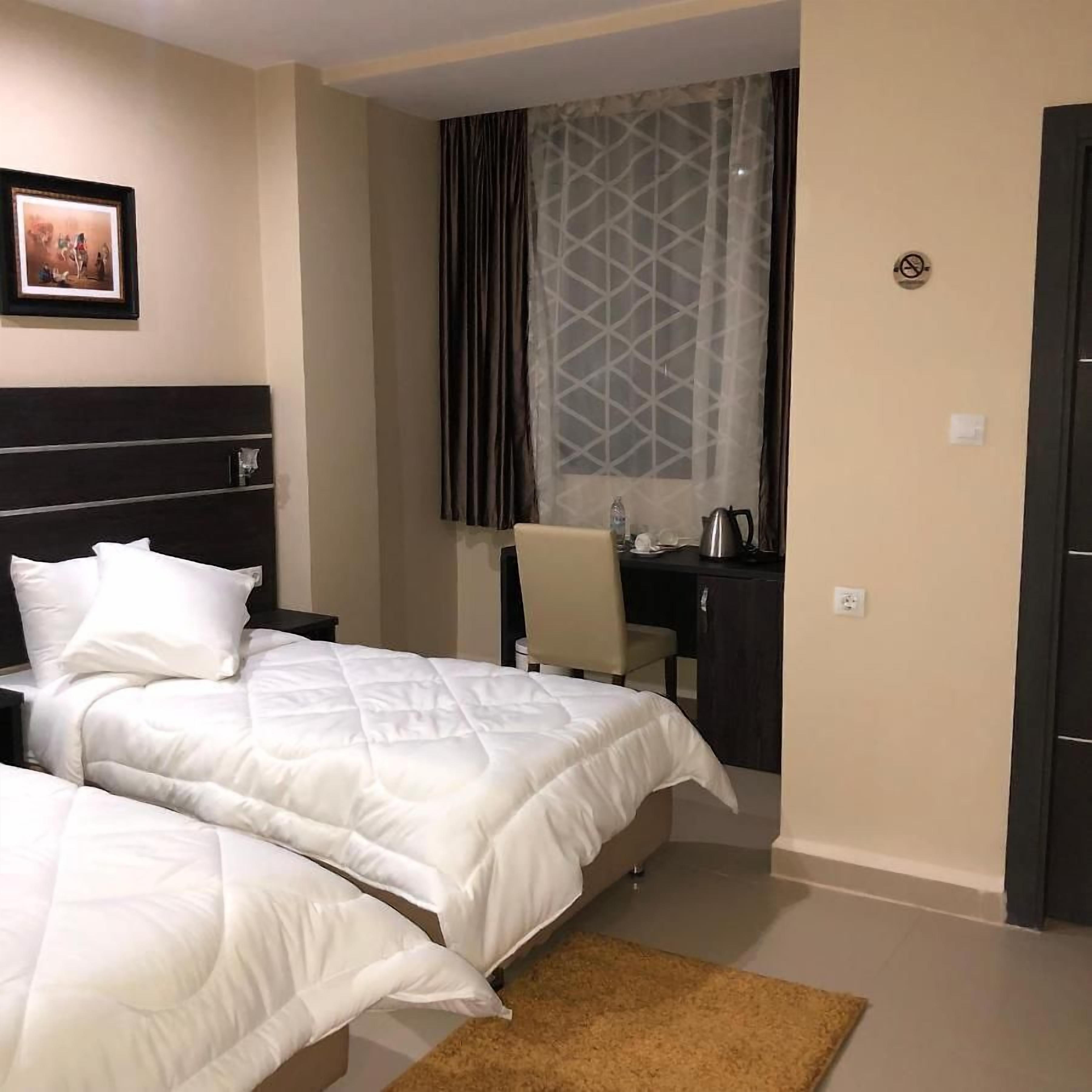 Habitación de hotel con dos camas, un escritorio, una silla, cafetera y ventana con cortinas.