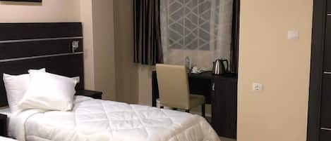 A hotel room with two beds, a desk, a chair, a coffee maker, and a window with curtains.