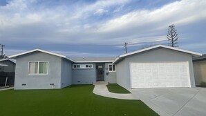 A two-story house with a garage, a front yard with artificial grass, and a clear sky.