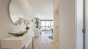 A modern hallway with a white console table, a large oval mirror, and white orchids. A potted plant is visible in the background. - Contemporary Residence B by Homie (Funchal)