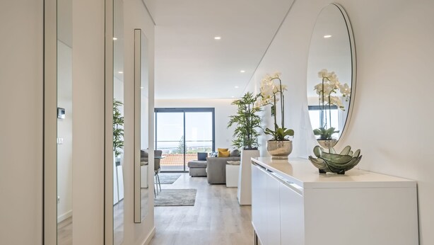 A modern kitchen with white cabinets, a large oval mirror, and decorative plants.