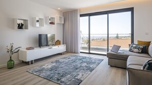 A modern living room with a large window, a flat-screen TV, a sofa, and a white console table.