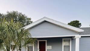 A single-story house with a red door, a small porch with a bench, and a mailbox.