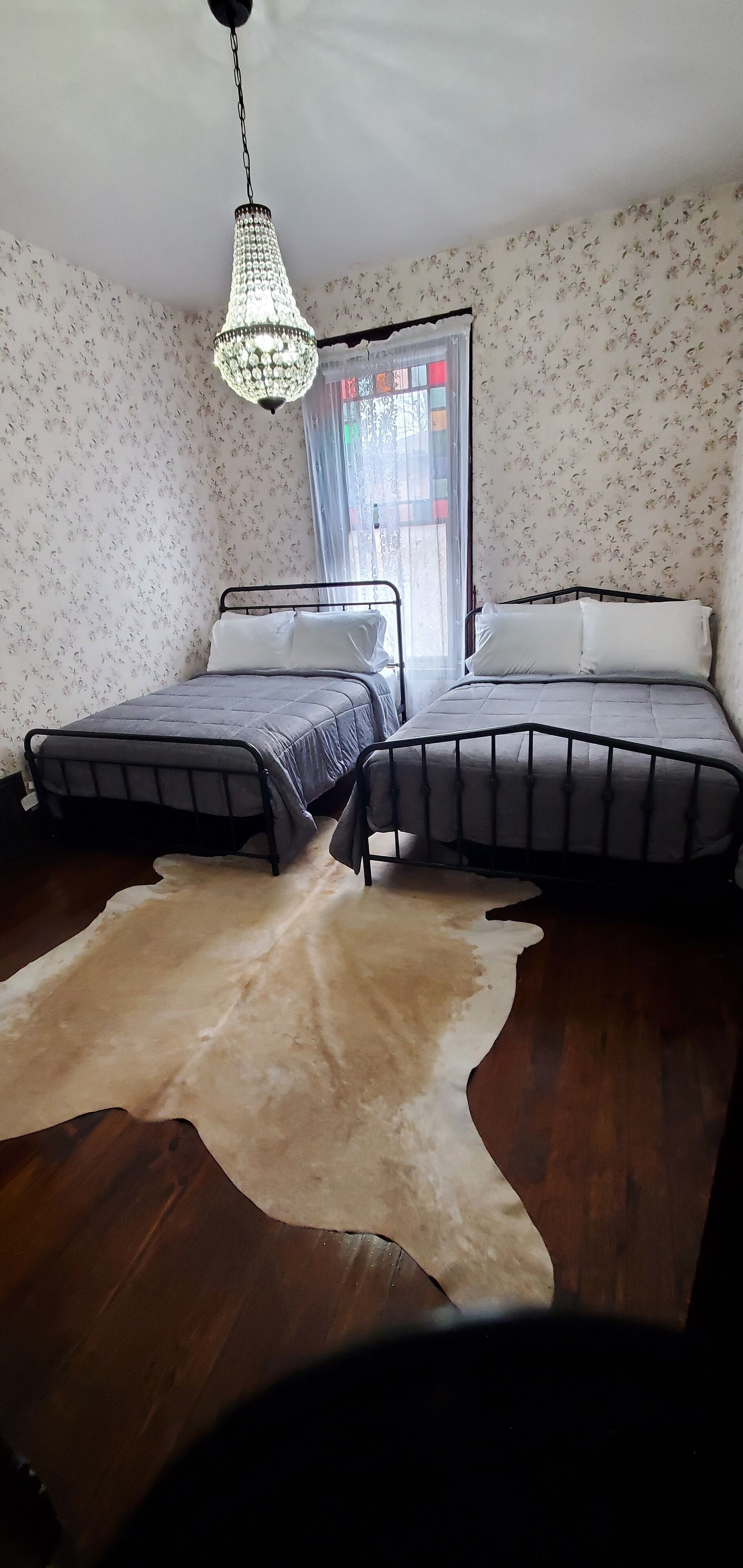 Un dormitorio con dos camas, una araña, papel tapiz floral y una alfombra de piel de vaca.