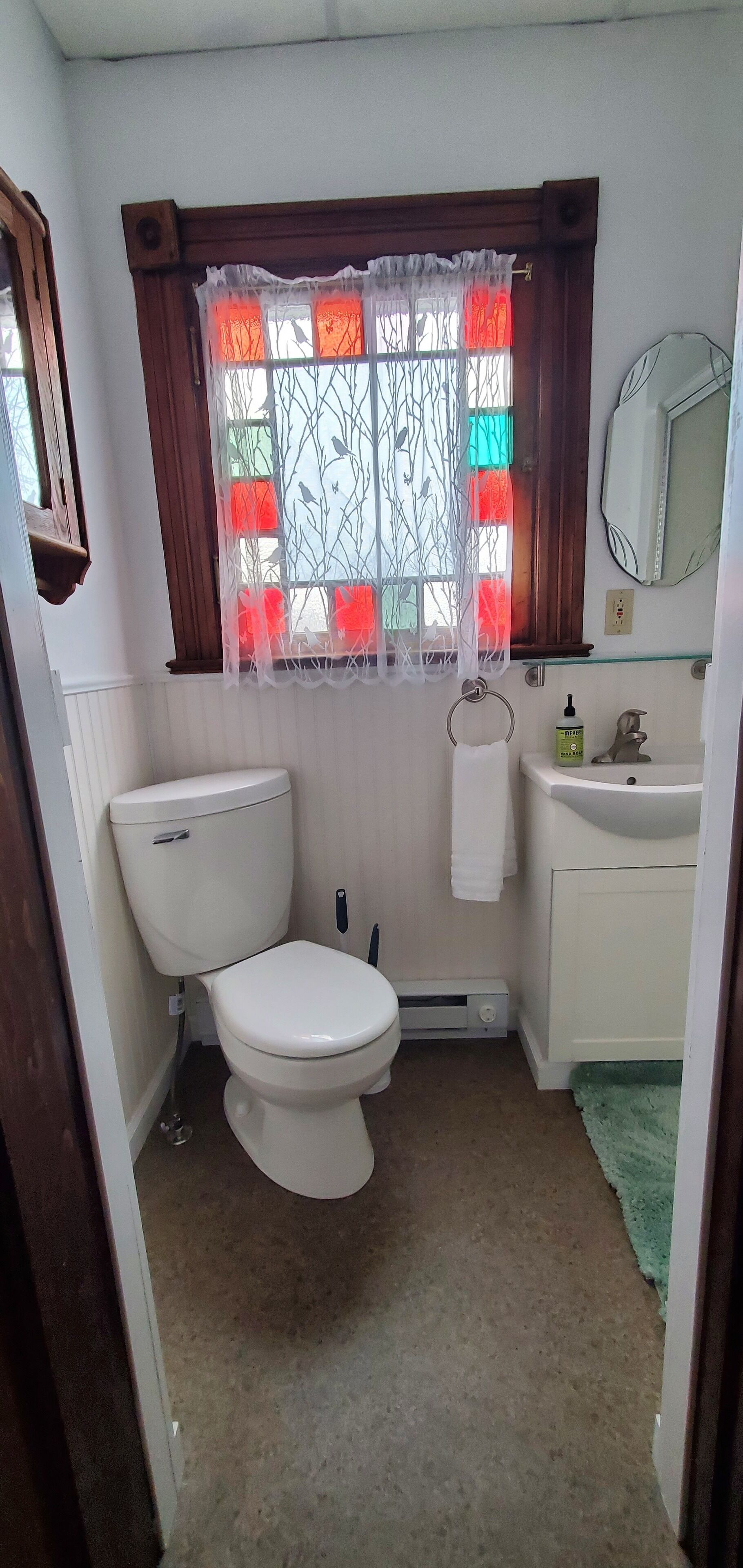 Un baño pequeño y limpio con inodoro, lavamanos y ventana con cortinas decorativas.