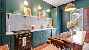 A kitchen with teal cabinets, a marble countertop, a stove, and pendant lighting. - Spectacular Queen Anne Victorian (Auburn)