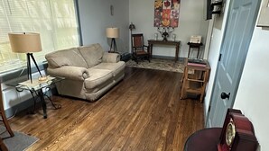 Ein Wohnzimmer mit einem beigefarbenen Sofa, einem Holztisch, einer Lampe und einem an der Wand montierten Fernseher.