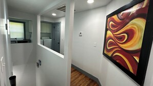 Ein Flur mit Holzboden, einem Gemälde an der Wand und einem durch eine geöffnete Tür einsehbarer Waschbereich.