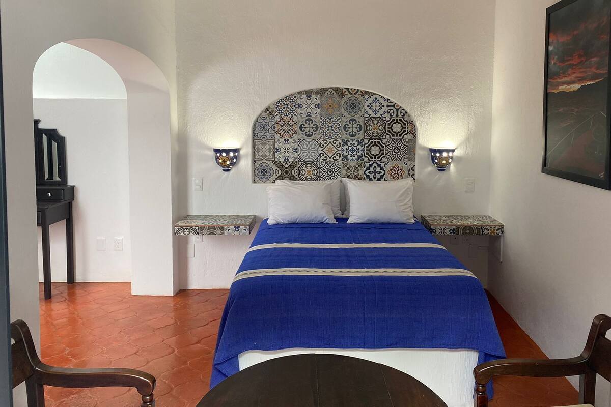 A bedroom with a patterned headboard, two bedside lamps, a blue bedspread, and a painting on the wall.