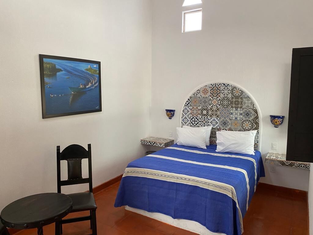Une chambre à coucher avec un lit, une chaise, une petite table et un tableau accroché au mur.
