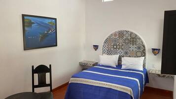 Un dormitorio con cama, una silla, una mesita y un cuadro en la pared.