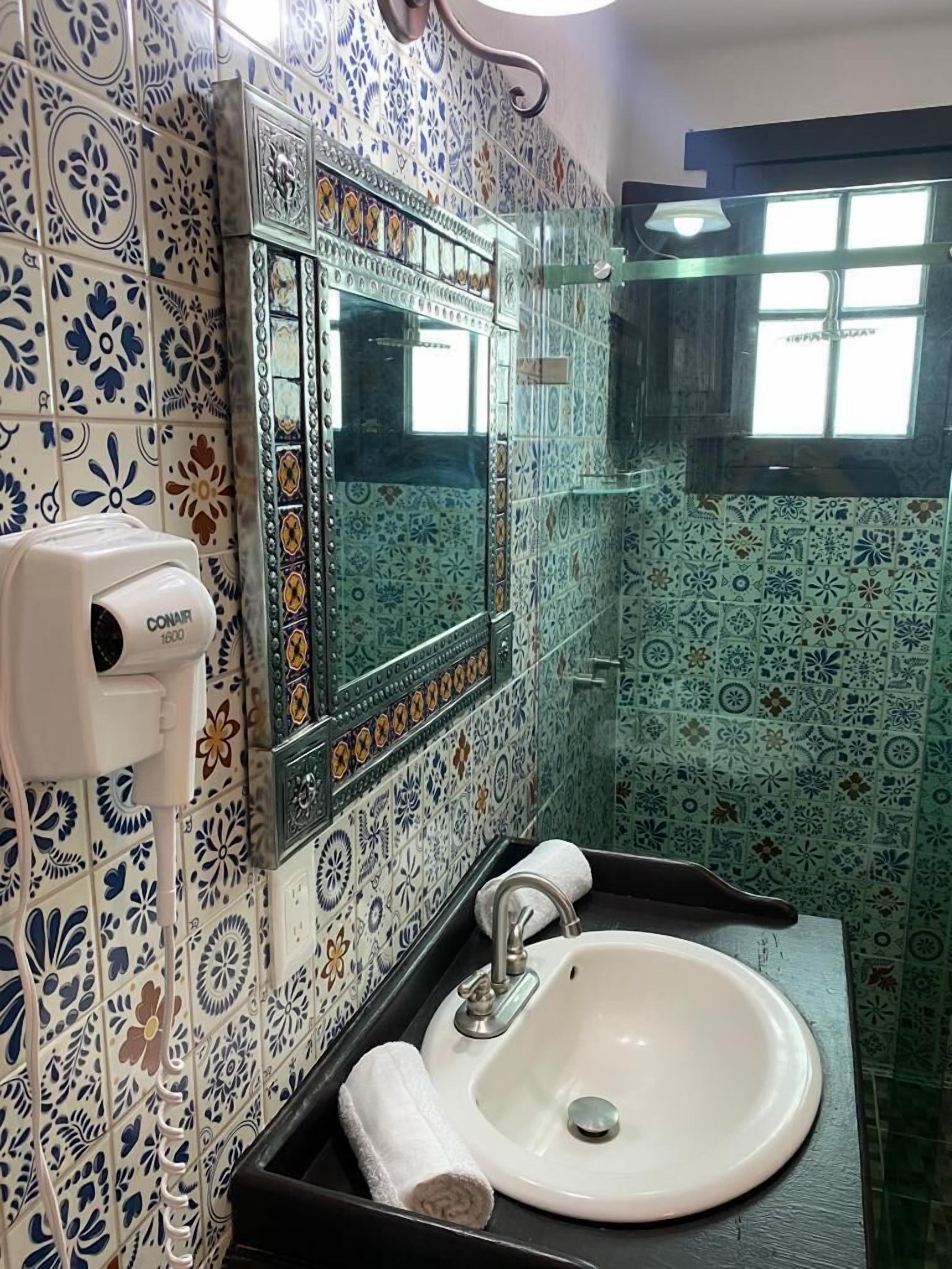 A bathroom with a white sink, a mirror, and a hand dryer. The walls are decorated with blue and white patterned tiles.