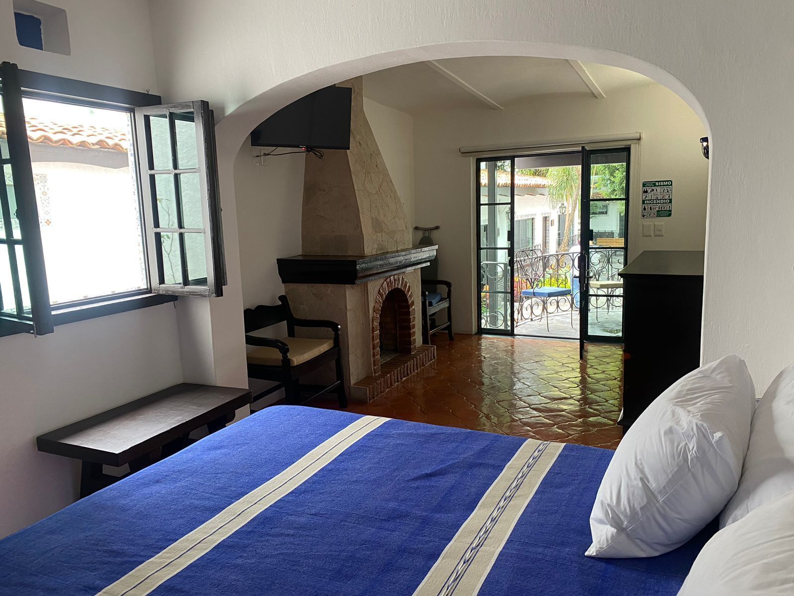 Una habitación de hotel con cama, chimenea, balcón con vistas y ventana.
