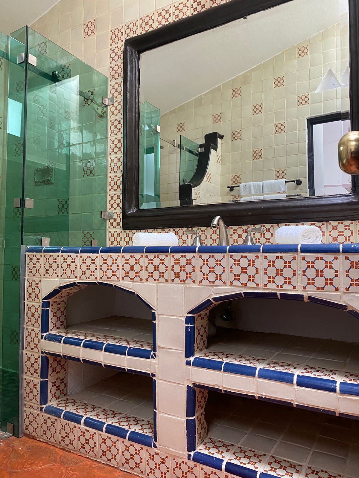 Une salle de bain avec une douche à parois de verre, un lavabo avec un miroir et des carreaux décorés.