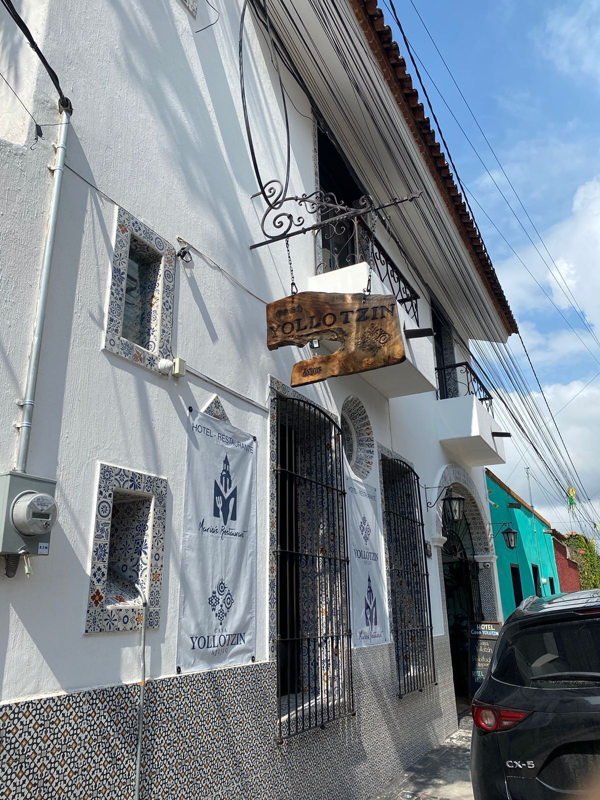 A building with a white facade, multiple windows, and a hanging sign that reads "YOLLOTZIN HOTEL RESTAURANTE".