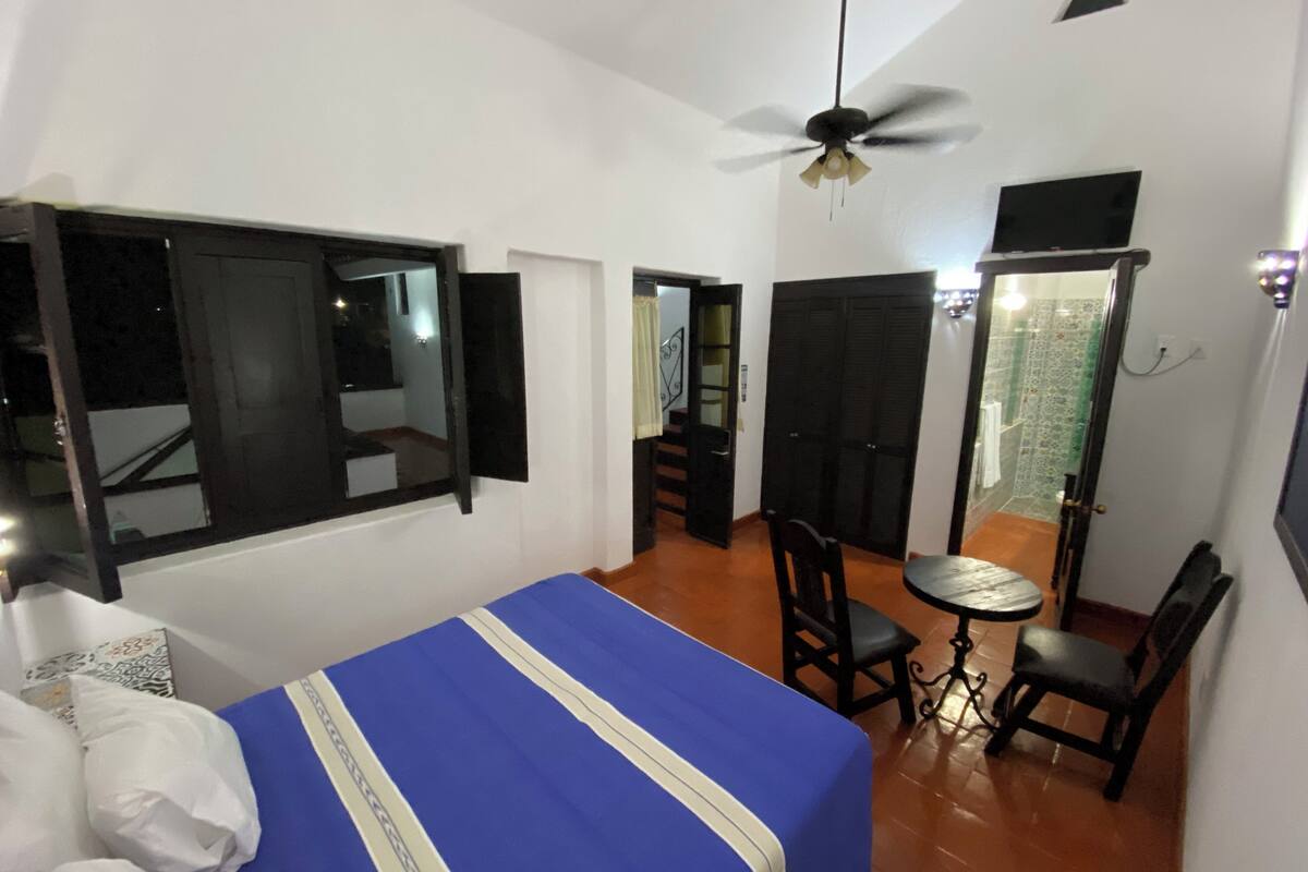 A bedroom with a bed, a ceiling fan, a window, a door, and a small table with chairs.