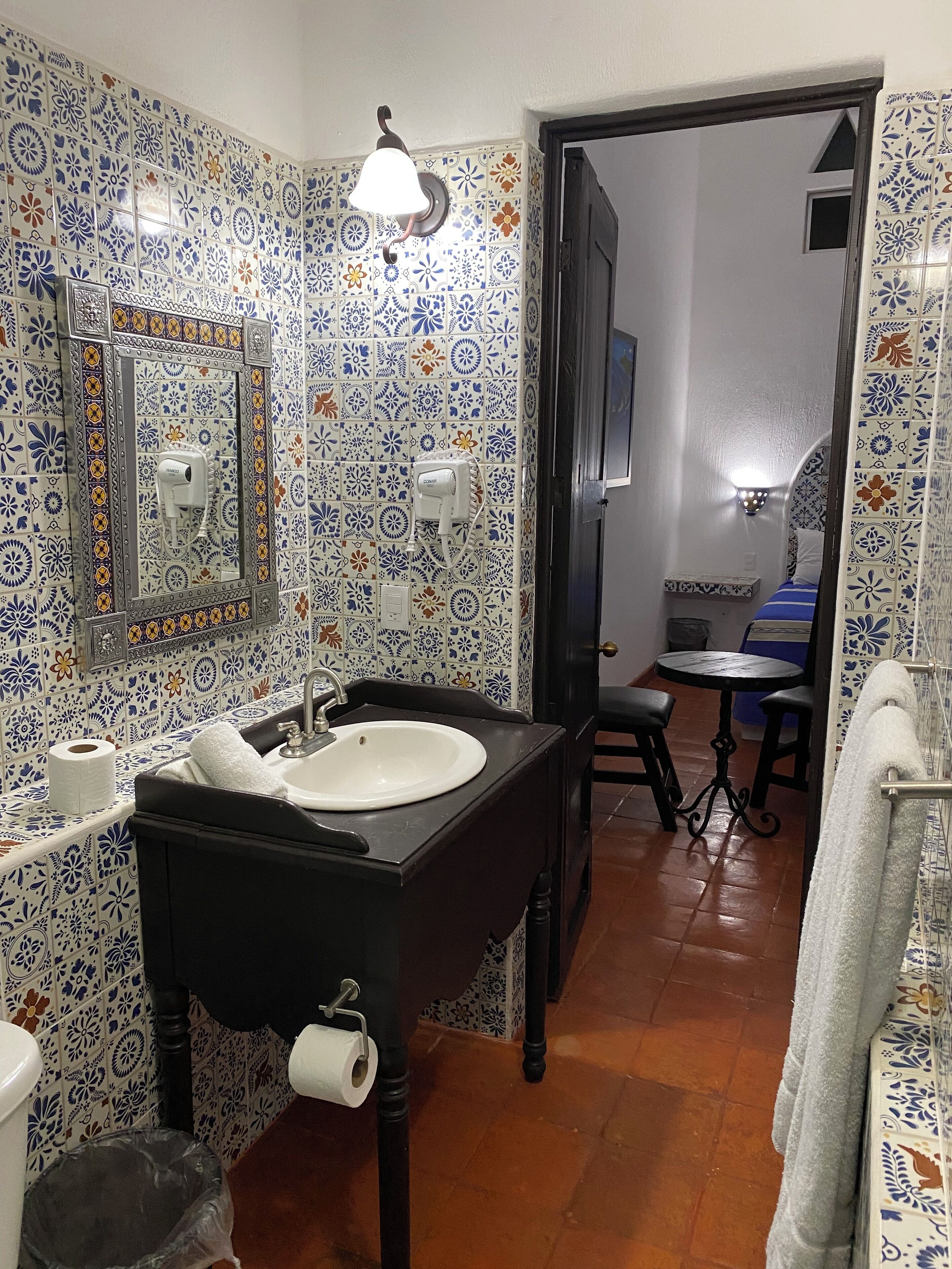 A bathroom with a sink, mirror, and hand dryer. There is a towel rack and a trash bin.