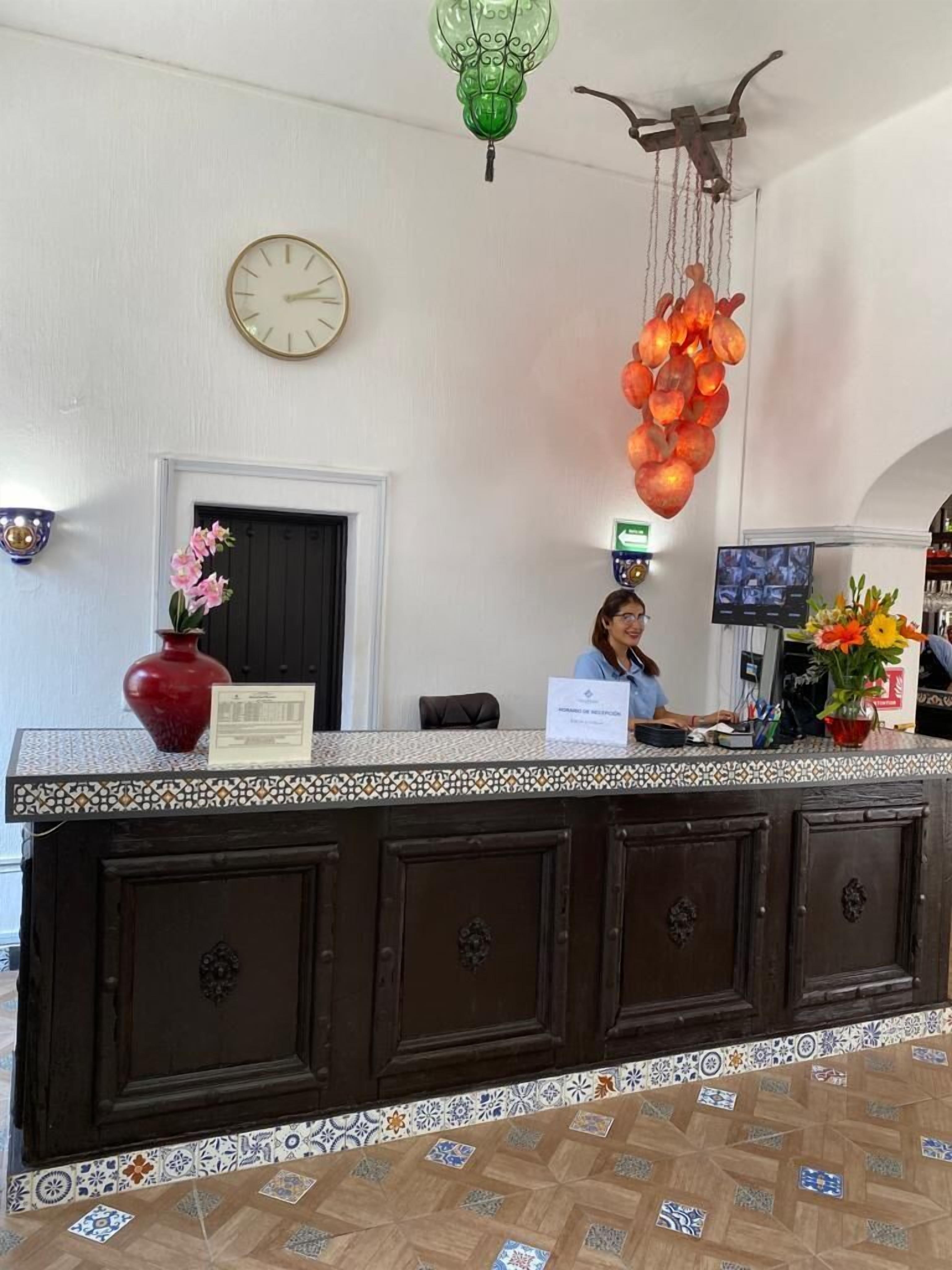 Una recepción con un reloj, un florero y una lámpara colgante.