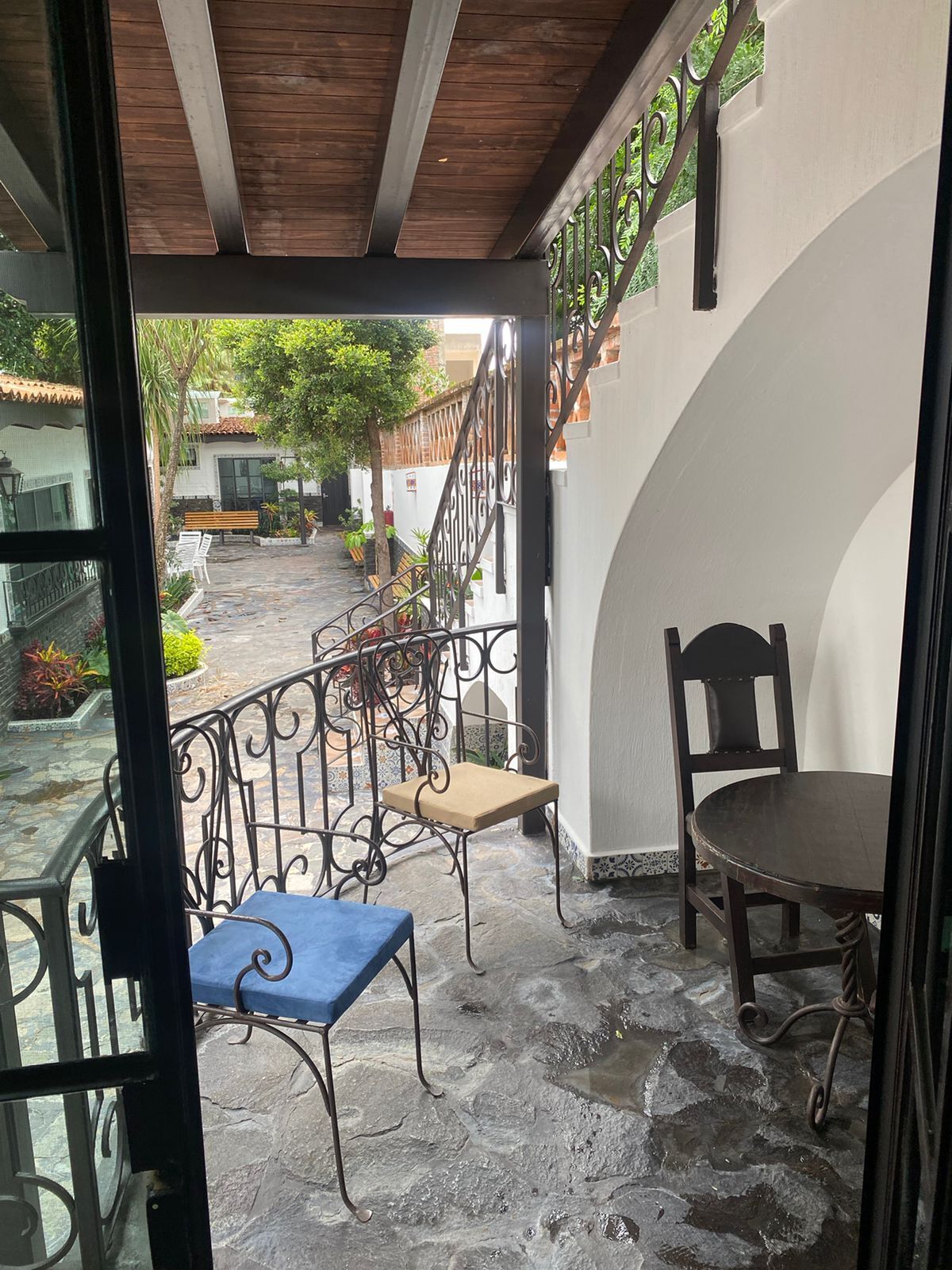 A stone-floored patio with a wooden ceiling, a metal railing, and a table with a chair.