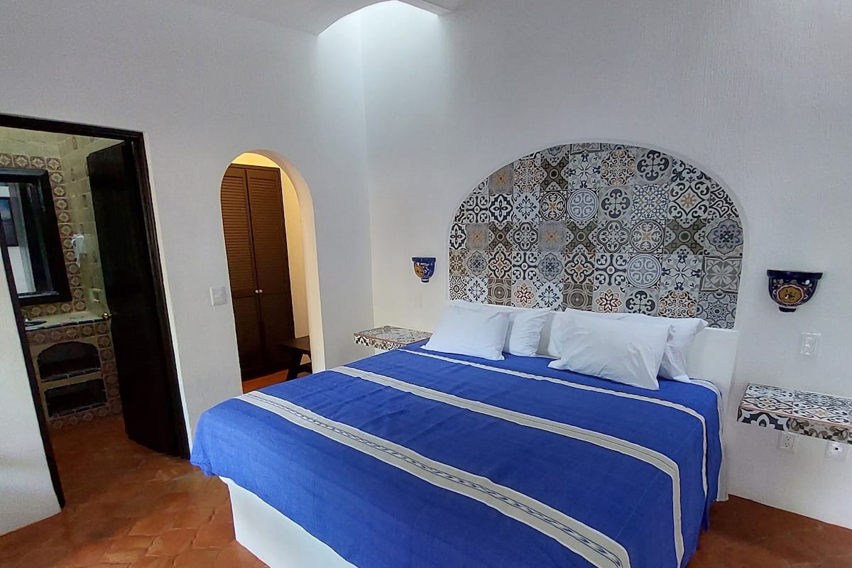A bedroom with a bed, a ceiling fan, a patterned headboard, and a tiled floor.