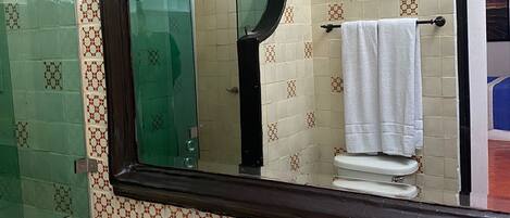 Un baño con un espejo grande, un lavabo con una pila decorativa y un box de ducha de vidrio.