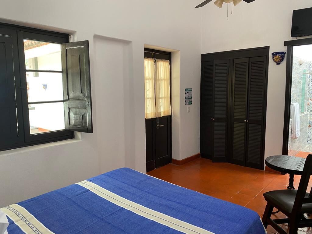 Un dormitorio con cama, ventana, puerta y una pequeña mesa con silla.