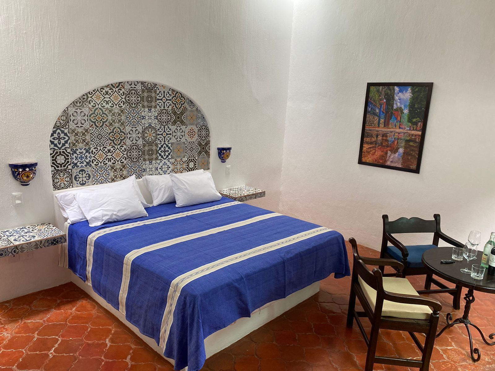 A room with a bed, a chair, a table, and a painting on the wall.