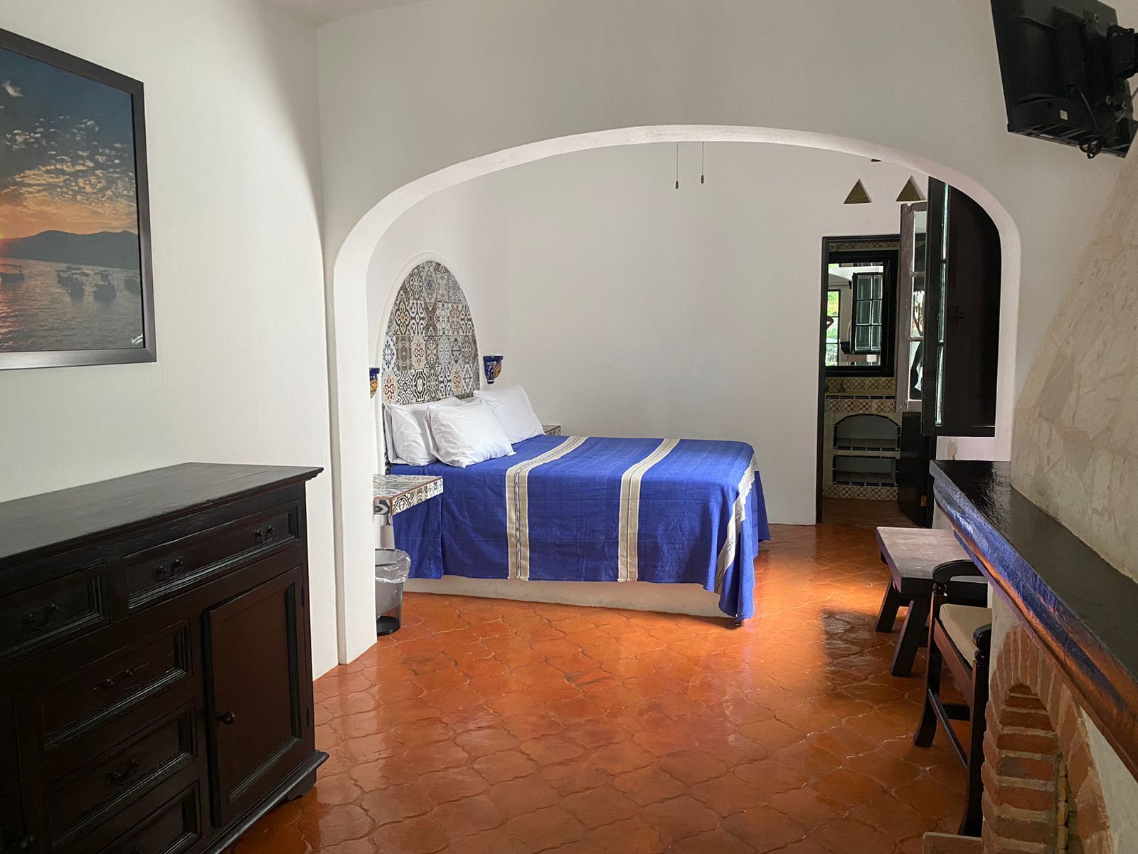 A bedroom with a bed, a dresser, a TV, and a bathroom visible through an archway.