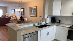 Een moderne keuken met witte kastjes, een roestvrijstalen vaatwasser, een granieten aanrechtblad en een geïntegreerde spoelbak.