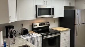 Een moderne keuken met witte kasten, een roestvrijstalen koelkast, een magnetron, een oven en een plafondventilator.