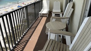 Een balkon met witte Adirondack-stoelen en uitzicht op een strand met parasols.