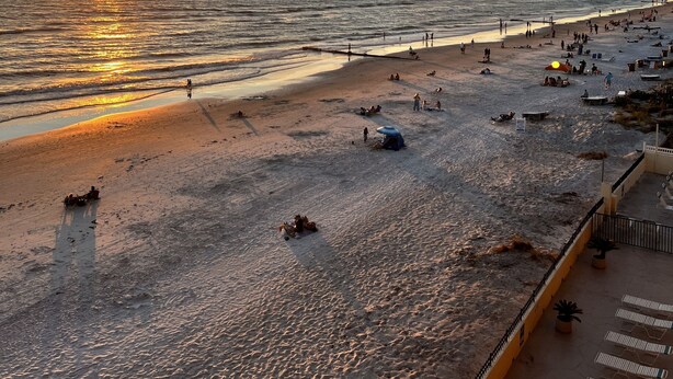 Een strand bij zonsondergang, met mensen en ligstoelen.