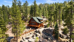 A cabin with a wooden deck, surrounded by trees and rocks.