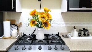 Une cuisine équipée d’une cuisinière à gaz, d’un four à micro-ondes et d’un vase rempli de tournesols, posé sur le plan de travail.