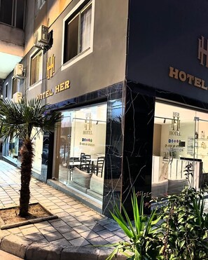 A hotel facade with large windows, a palm tree, and a black marble border. - Hotel HER (Vlorë)