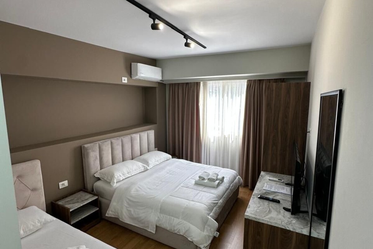 A modern hotel room with a large bed, a desk with a flat-screen TV, and a built-in air conditioning unit.