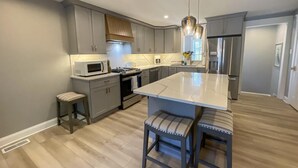 A modern kitchen with grey cabinets, a central island with bar stools, a microwave, stove, and a refrigerator. - 905 Page Street Cape May (Cape May)