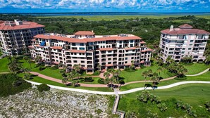 Un hôtel à plusieurs étages doté d’une cour intérieure, entouré d’une végétation luxuriante et offrant une vue sur la plage.
