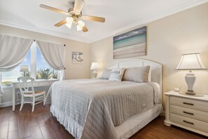 Una camera da letto con un letto, una scrivania, una sedia, un comodino, una lampada e una ventola a soffitto.