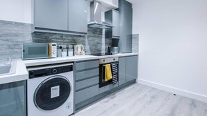 Een moderne keuken met grijze kastjes, een ingebouwde magnetron, een koffieapparaat en een wasmachine.
