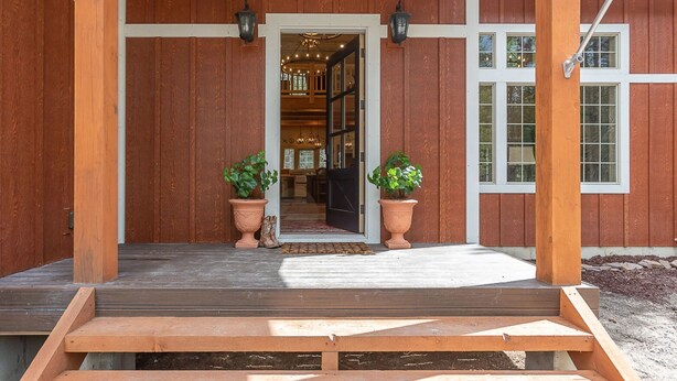 A wooden porch with a bench, potted plants, and a door leading to an interior space with a chandelier. - Uncle Chris' Cabin (Island Park)
