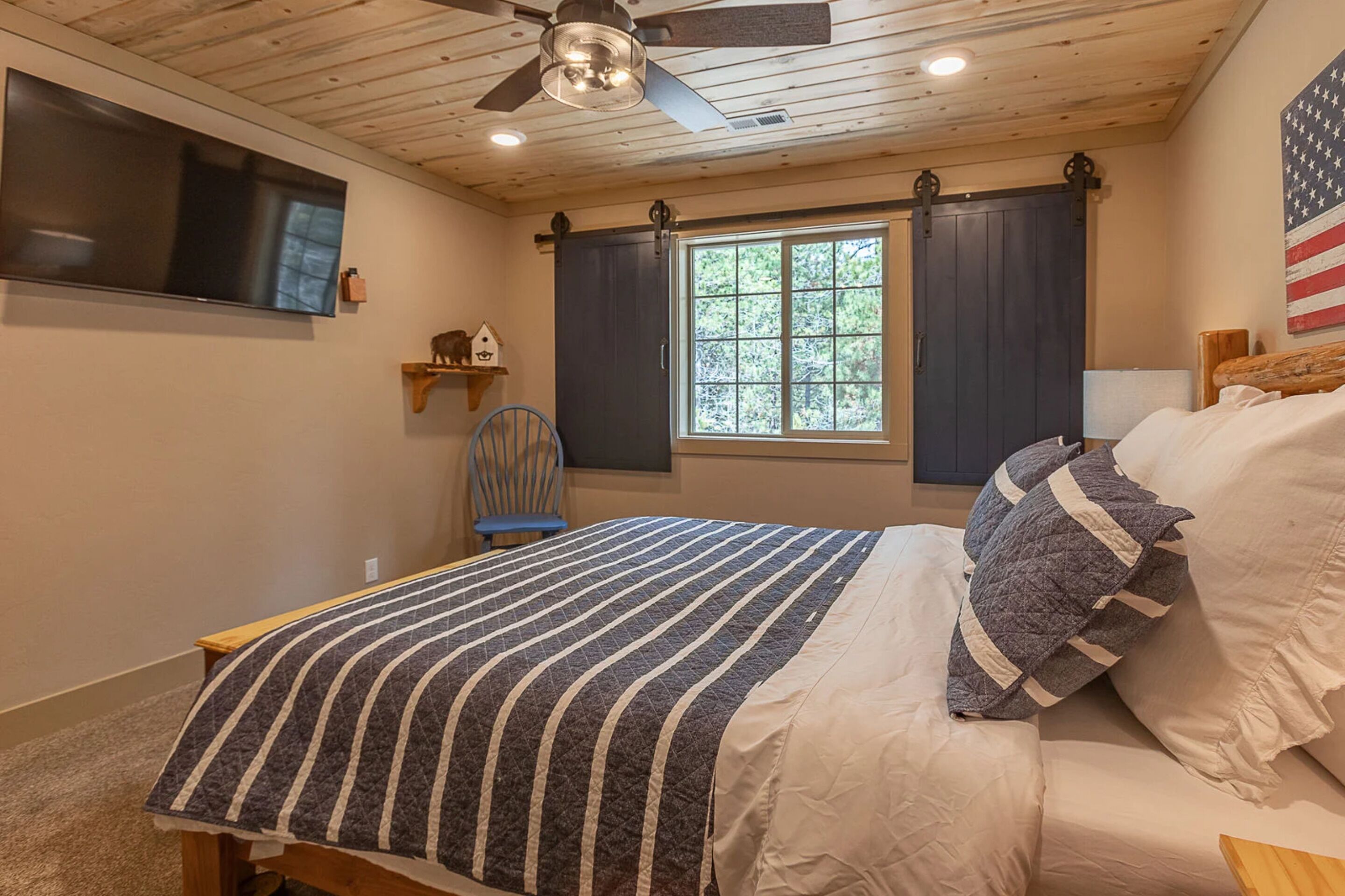 A bedroom with a bed, a ceiling fan, a TV, a window with curtains, and a wall-mounted shelf.