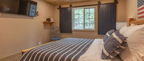A bedroom with a bed, a ceiling fan, a TV, a window with curtains, and a wall-mounted shelf.