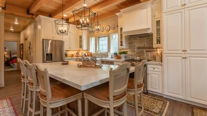 A spacious kitchen with a large island, white cabinetry, and a stone fireplace. - Uncle Chris' Cabin (Island Park)